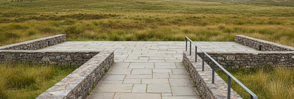 Wide flagstone terrace between low dry stone walls, a dark metal handrail on the right, open moor grass beyond